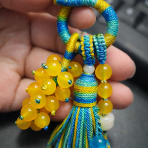 handwoven tassel pendant made with jade cord and yellow bead cluster on dark background